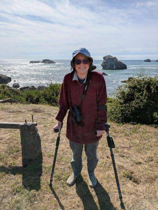 Person smiling with crutches by the ocean.
