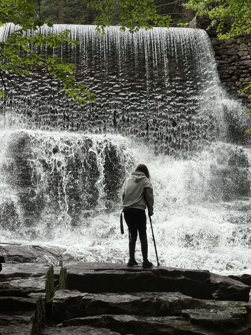Person standing near large cascading waterfall.