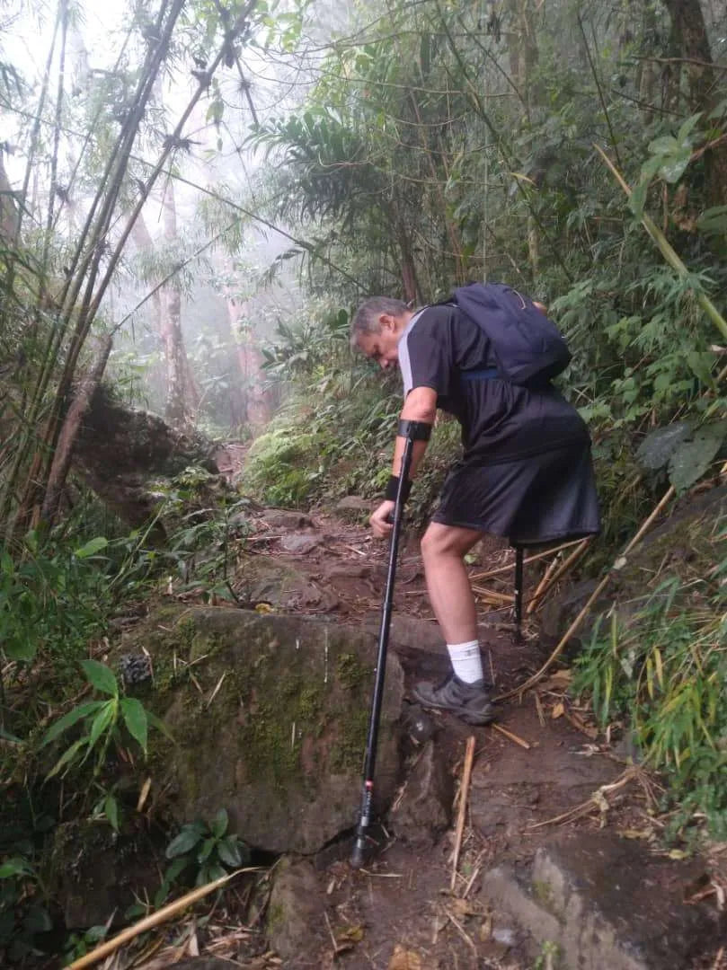Man with crutch hiking on forest trail.