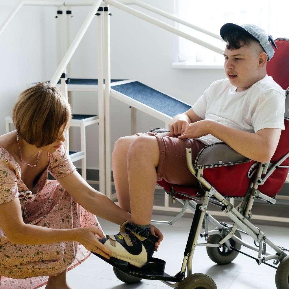 Woman adjusting shoe on child in wheelchair.