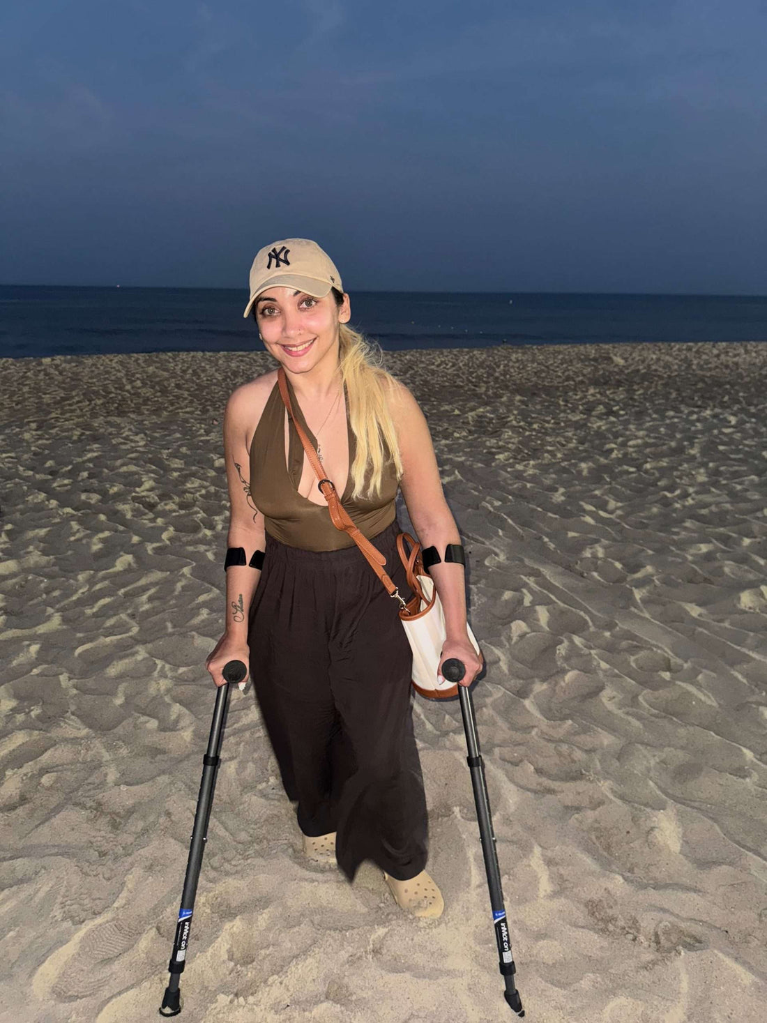 Person with crutches smiling on a beach at night.