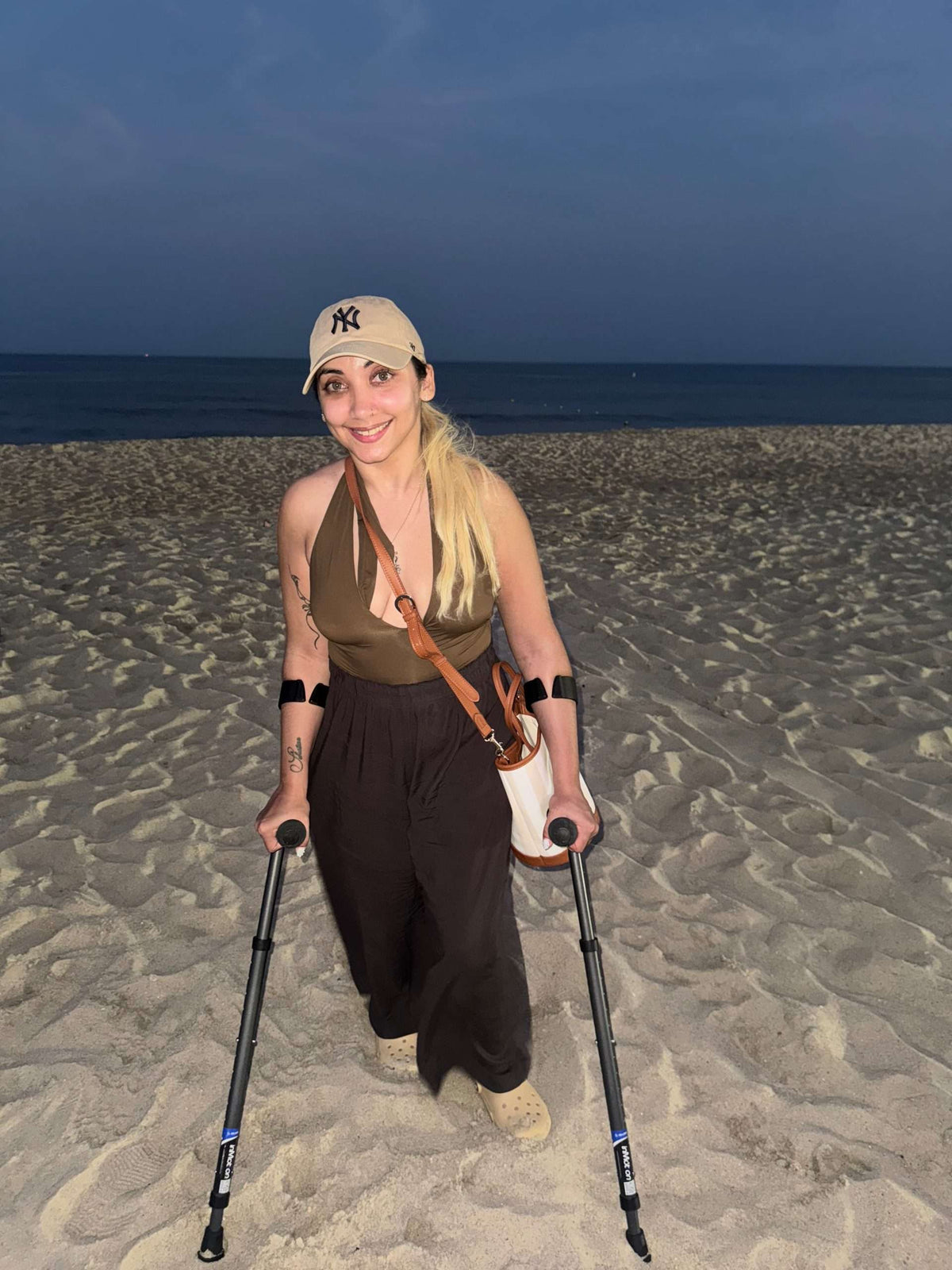 Person with crutches smiling on a beach at night.