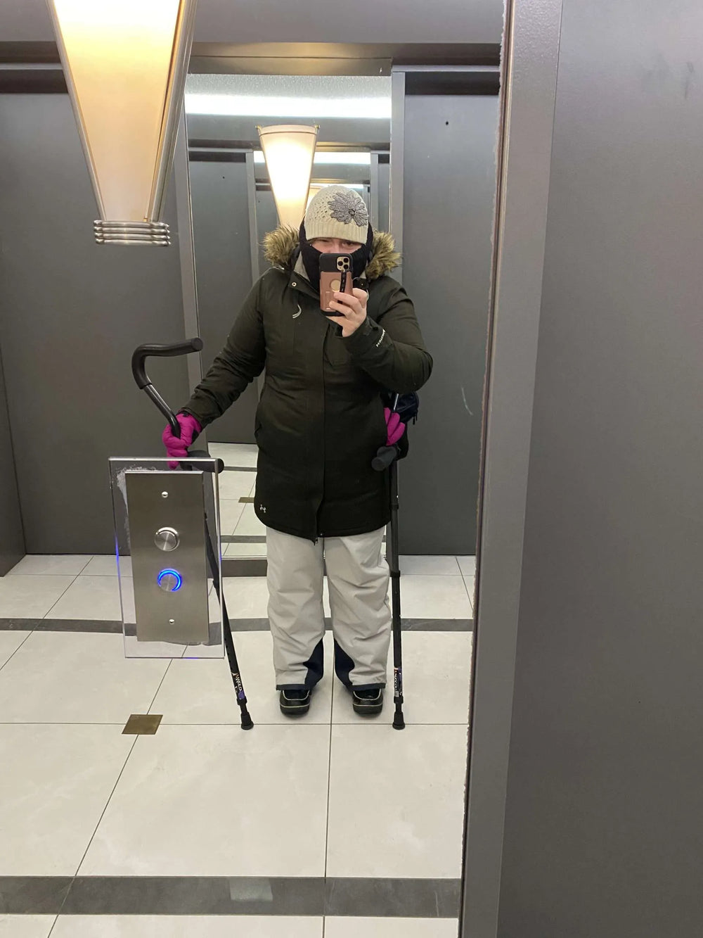 Person in winter clothes using crutches in elevator mirror.