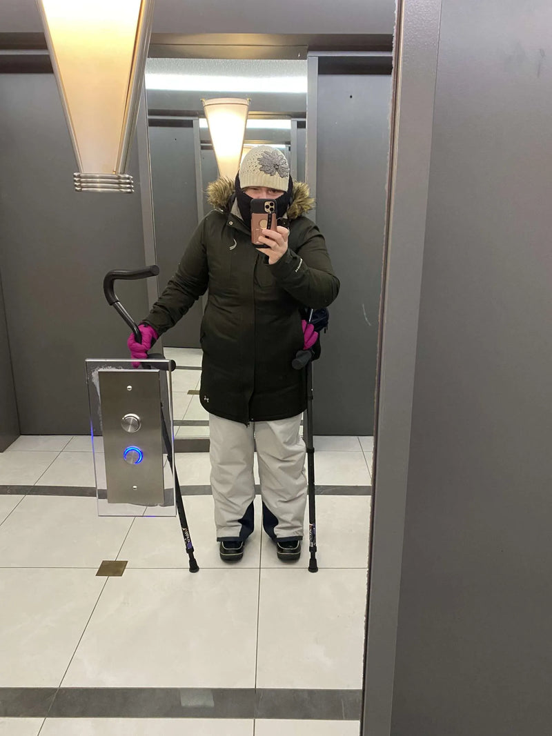 Person in winter clothes using crutches in elevator mirror.