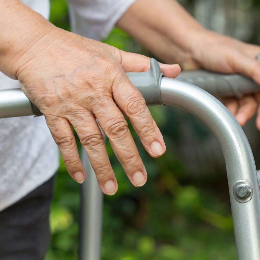 Elderly hand gripping a walker for support.