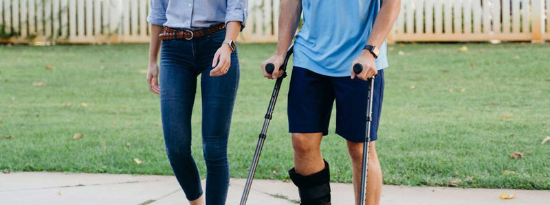 Person on crutches walking outside with companion.